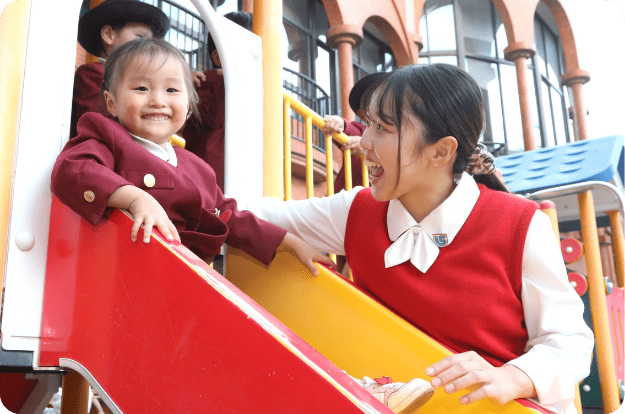 すべり台で楽しそうに笑う園児と先生の様子