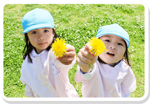 たんぽぽを手に持って笑顔で見せる園児の様子